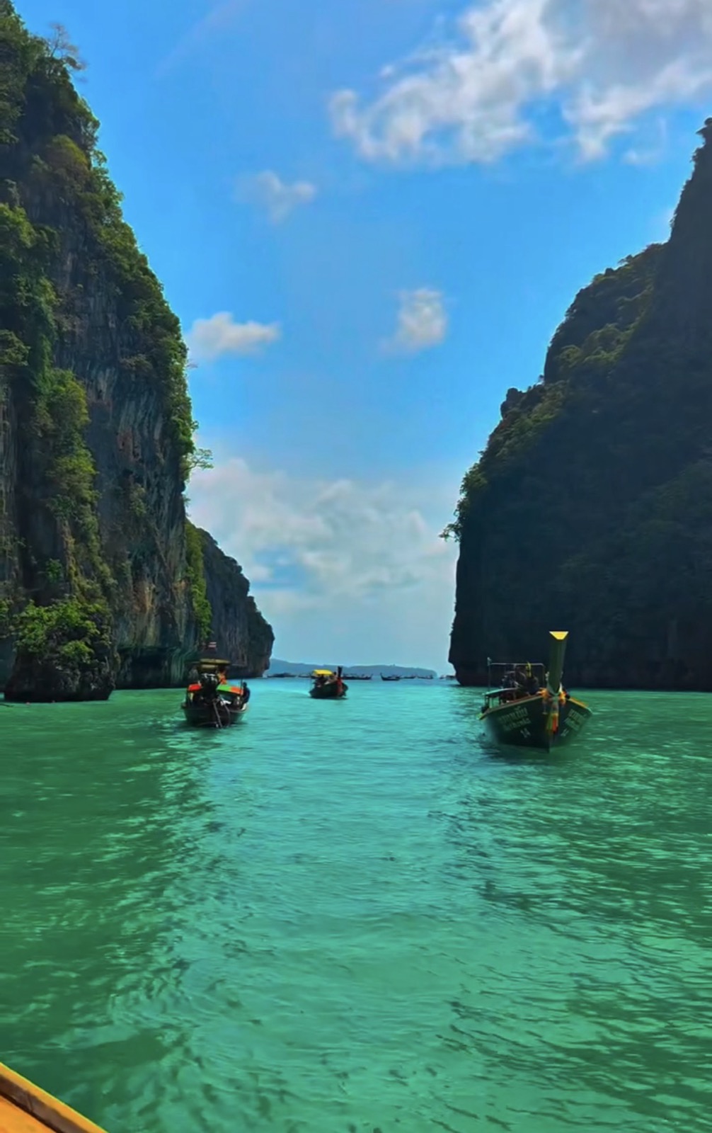 Longtail boats crossing calm turquoise water between limestone cliffs on a Phuket island trip, with cloud building overhead