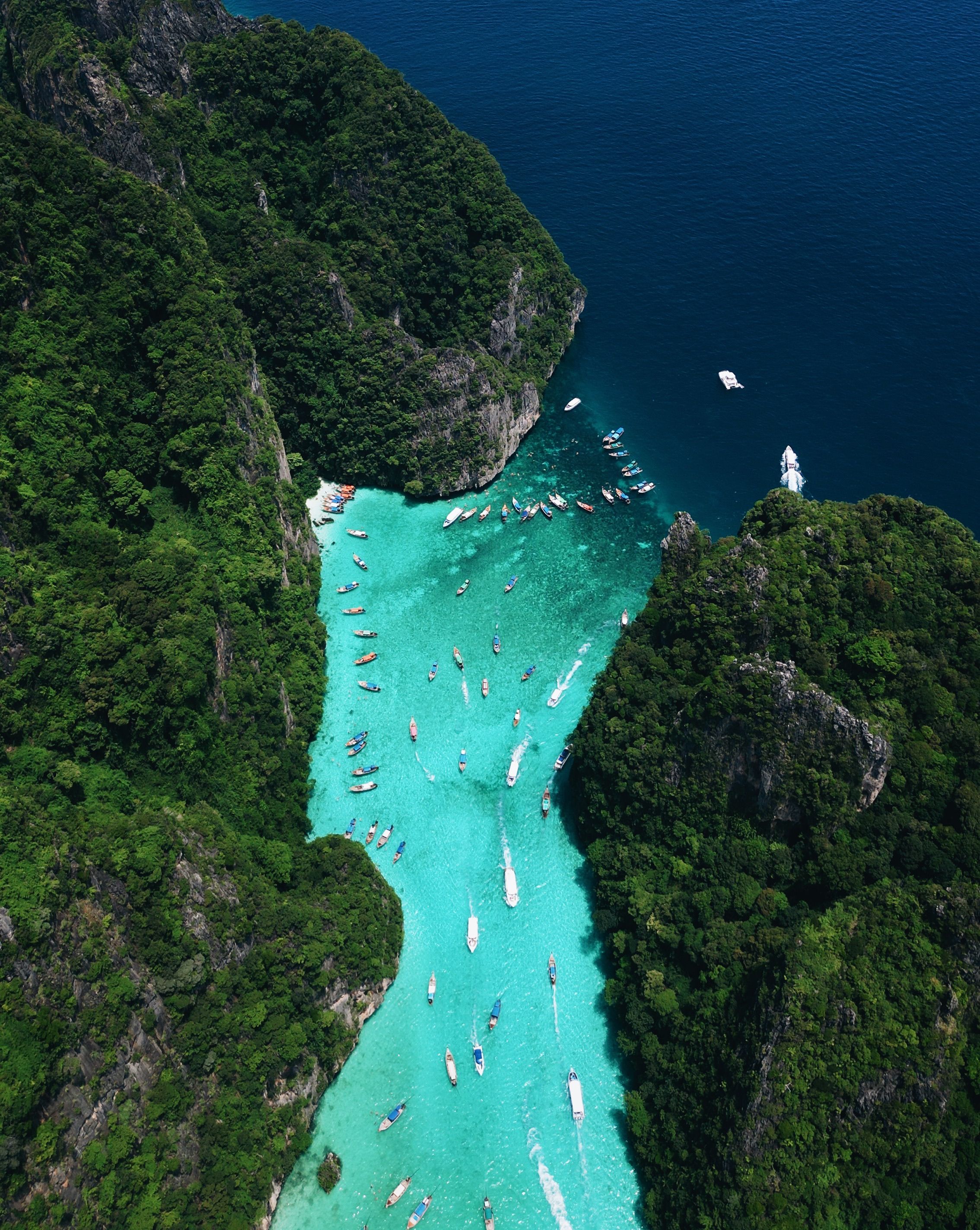 Aerial view of turquoise Pileh Lagoon between limestone cliffs, Phi Phi Islands, with longtail boats anchored in the bay